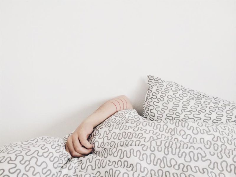 An arm resting on a patterned pillow in a bright bed